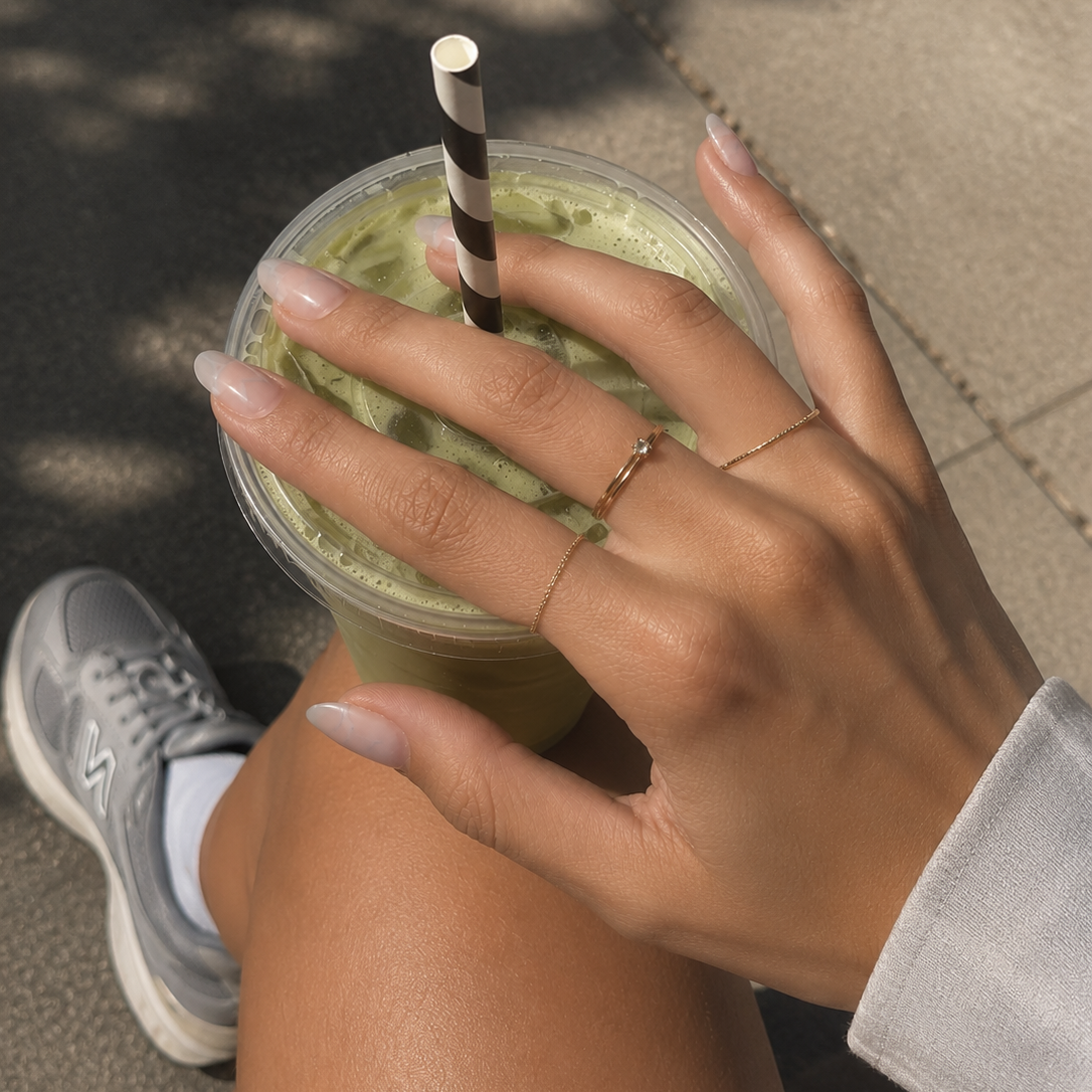 Hand holding a green smoothie with a straw on a sidewalk