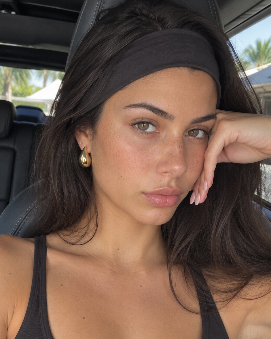 A woman with long dark brown hair wearing a black athletic headband and a black tank top, sitting inside a car and looking at the camera.